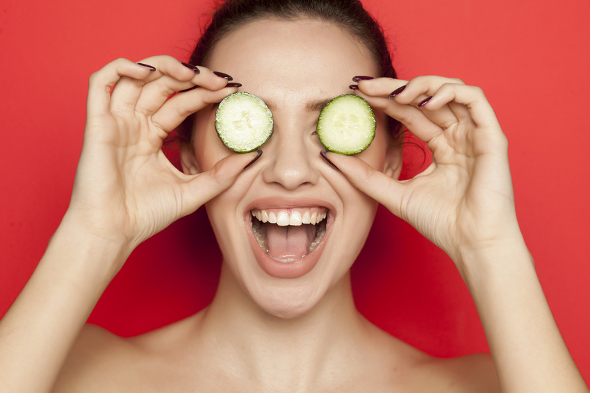 Happy young woman posing with slices of oranges on her face on red background